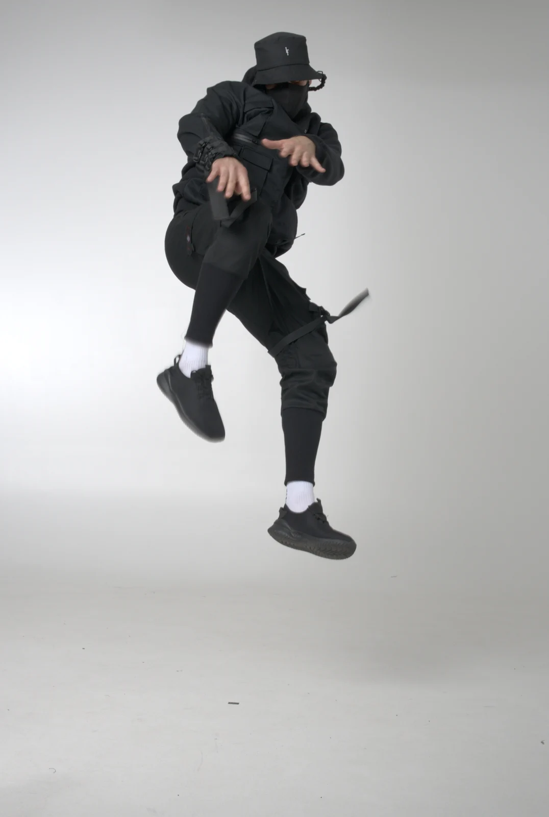 An all-black LF hooded outfit photographed mid-jump against a light studio background
