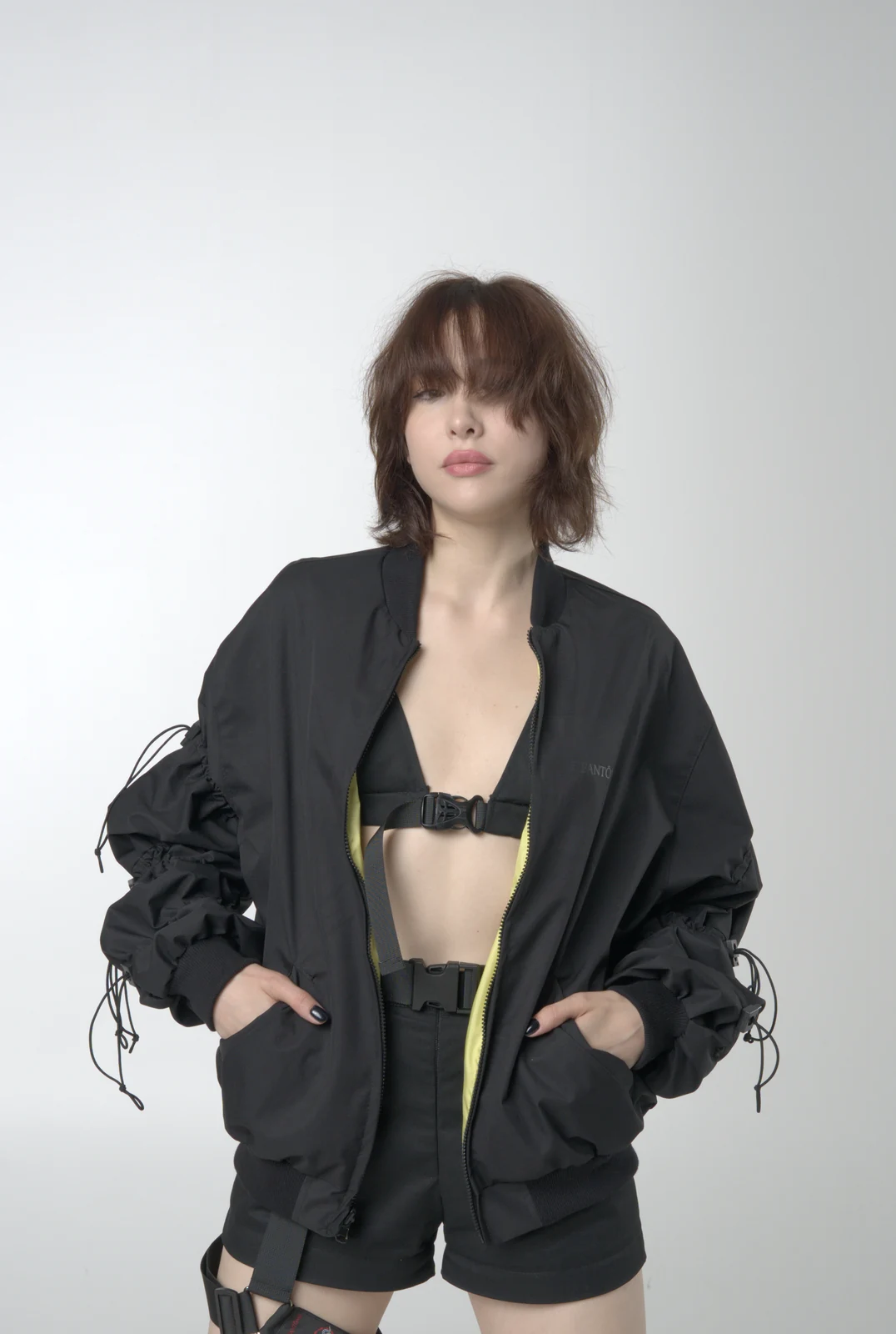 An LF black bomber jacket worn open over a buckle-fastened cropped top, with a contrasting lining edge