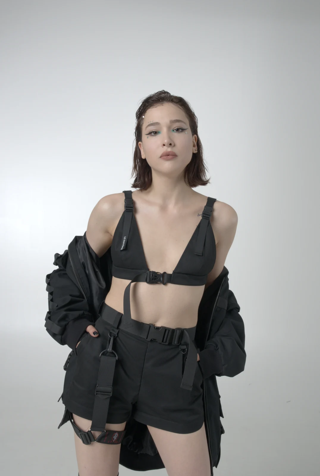 An LF black bomber jacket worn open over a buckle-front top and high-waisted shorts